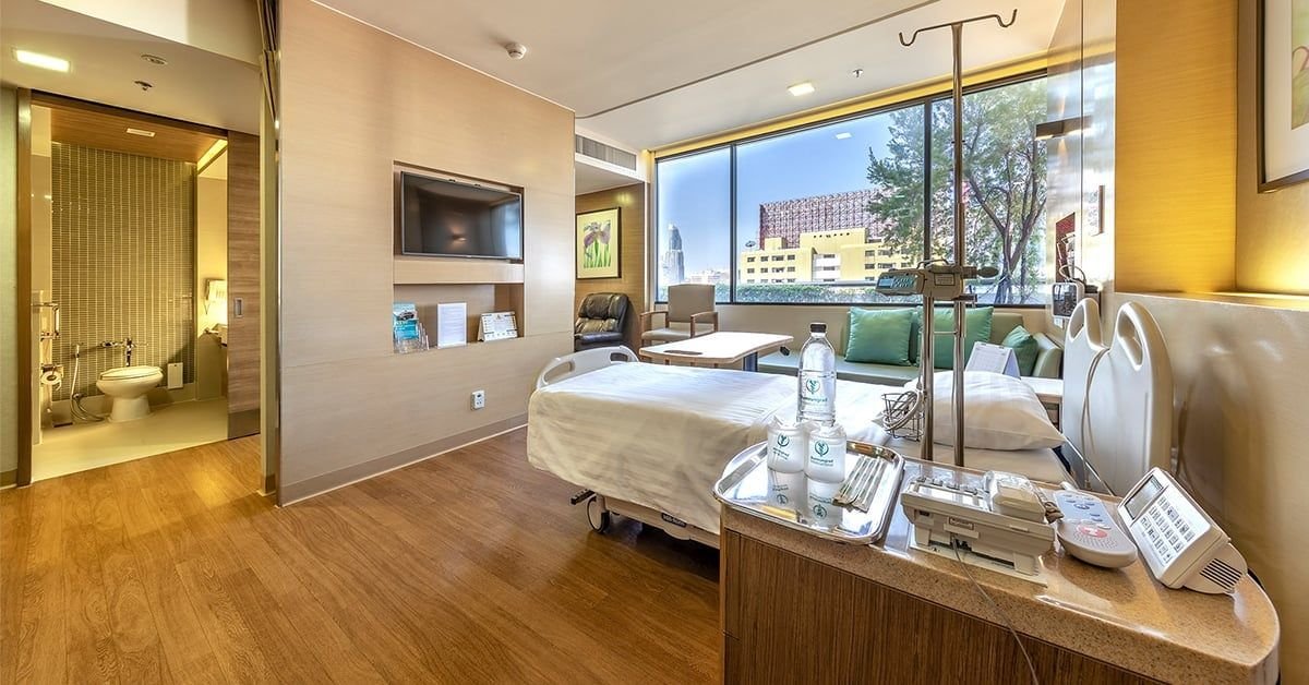 A private inpatient room at Bumrungrad International Hospital, with a hospital bed and a window over central Bangkok