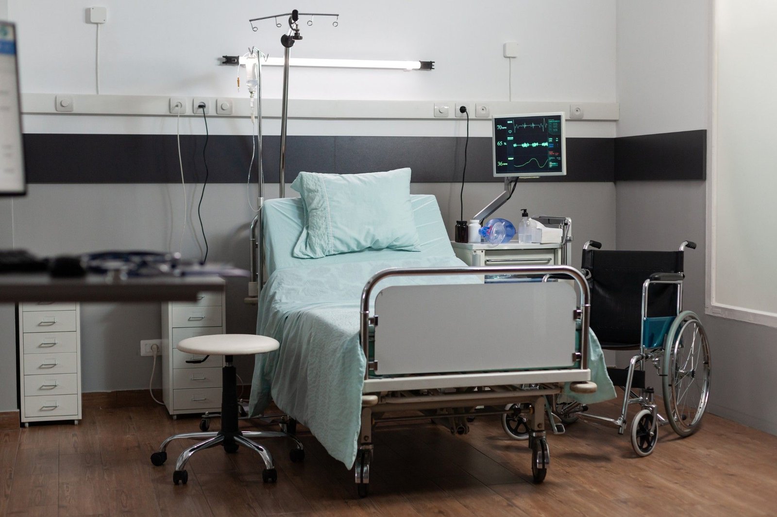 A single-bed inpatient room with a monitor and wheelchair beside the bed