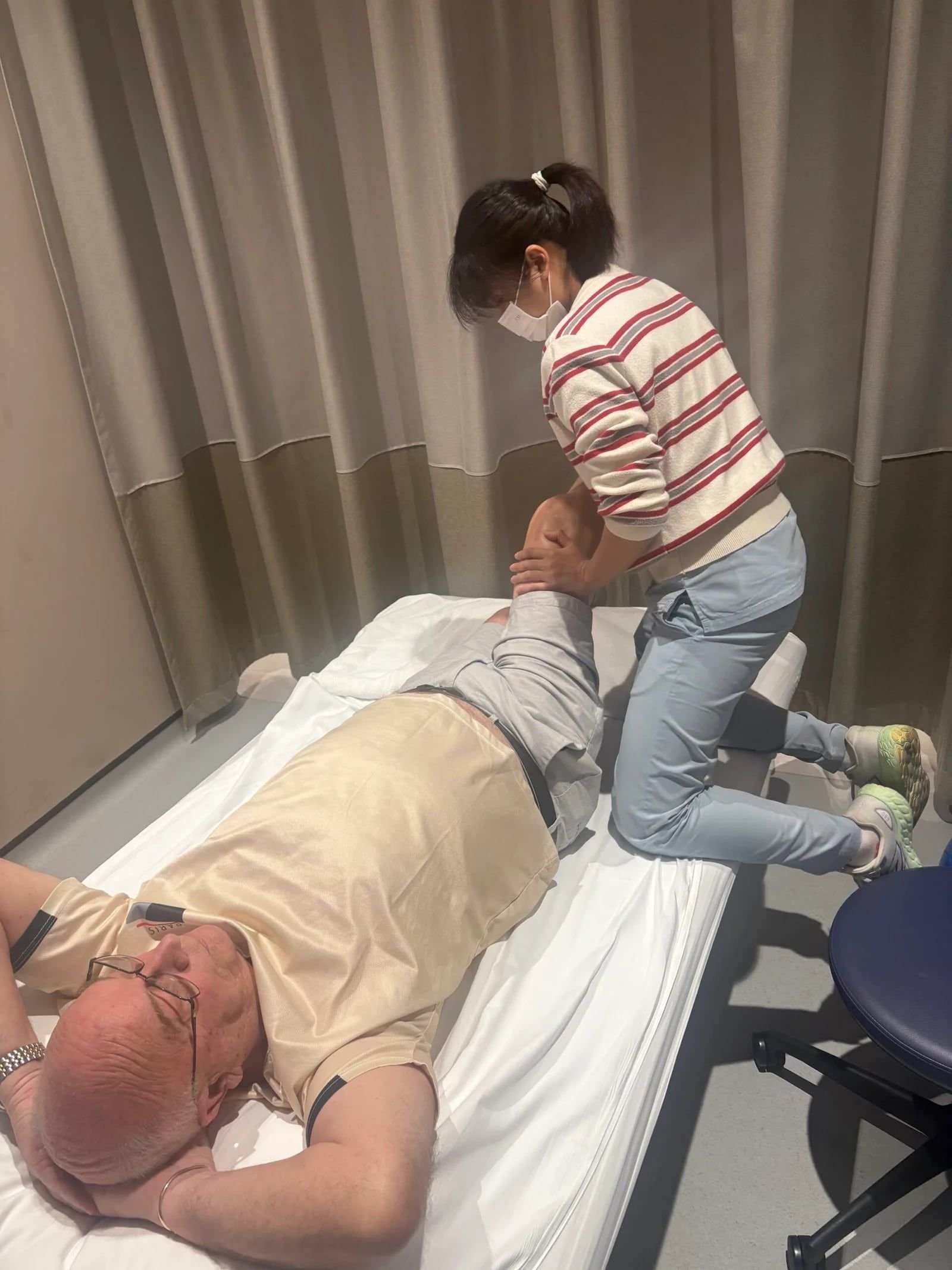 Steven Parker lying on a treatment bed while a therapist bends and supports his knee during physiotherapy